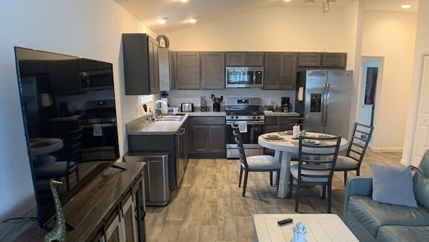 A modern kitchen with dark cabinets, a central island, and a dining area with a white table and chairs.