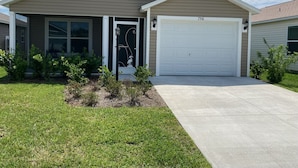 A single-story house with a garage, a front door with a decorative glass panel, and a small garden area with shrubs.