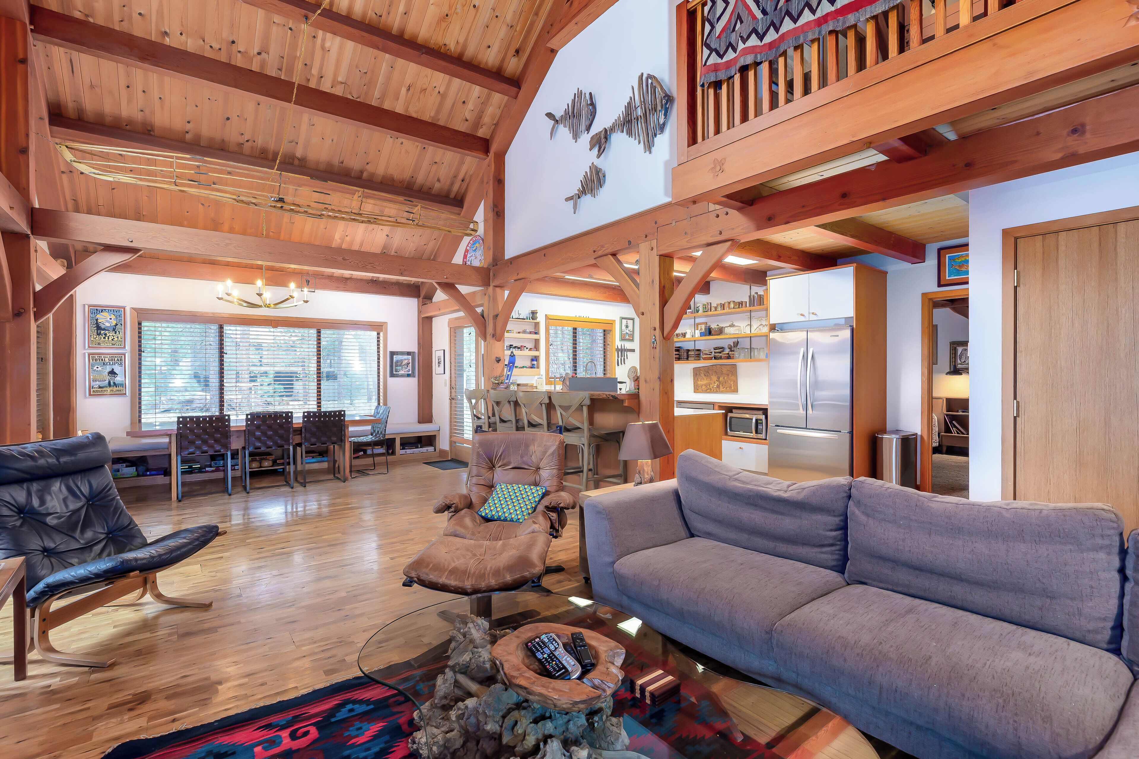 A spacious living area with a wooden ceiling, a grey sofa, a leather recliner, and a dining area with a table and chairs.