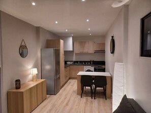 A modern kitchen with wooden cabinets, a stainless steel refrigerator, a dining table with chairs, and a washing machine.