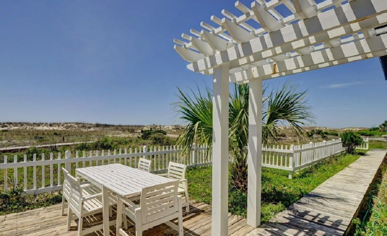 Eine Holzterrasse mit einer weißen Pergola und einem Tisch mit Stühlen.
