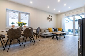 Un salon moderne comprenant un canapé, des fauteuils, une table à manger et un coin cuisine.