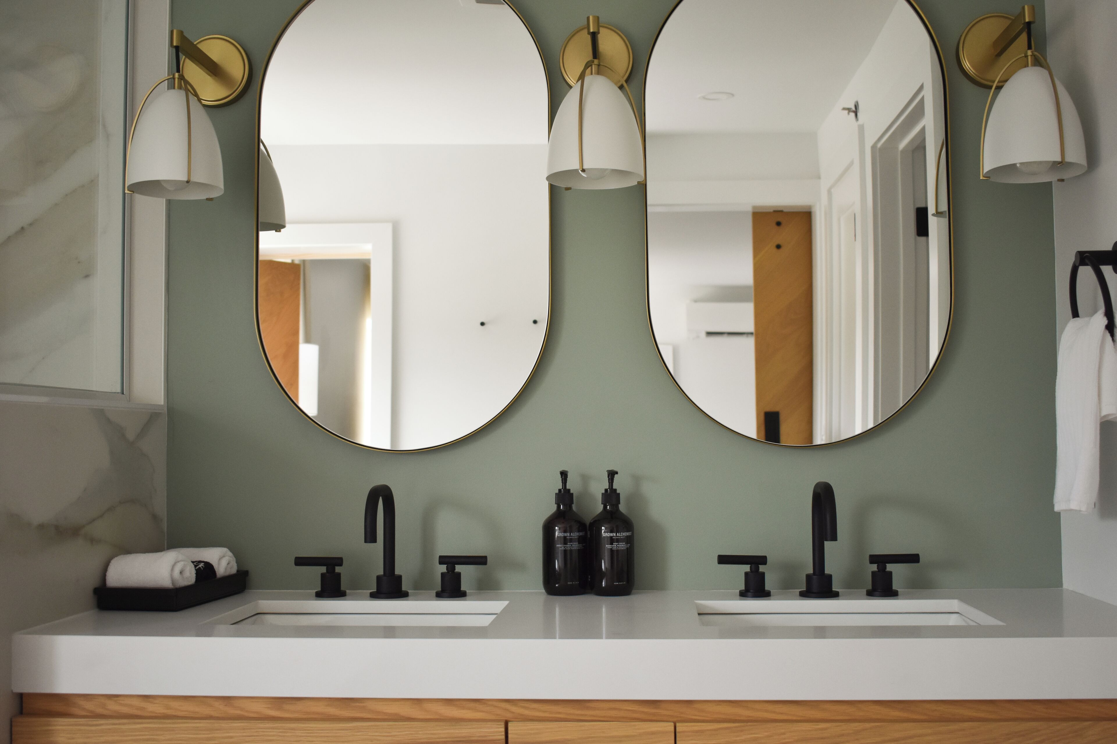 Un baño con lavamanos doble, dos espejos y tres luces empotradas.