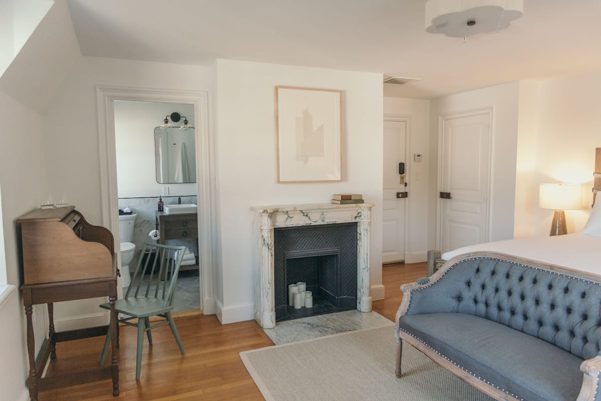 A bedroom with a bed, a fireplace, a piano, and a chair.