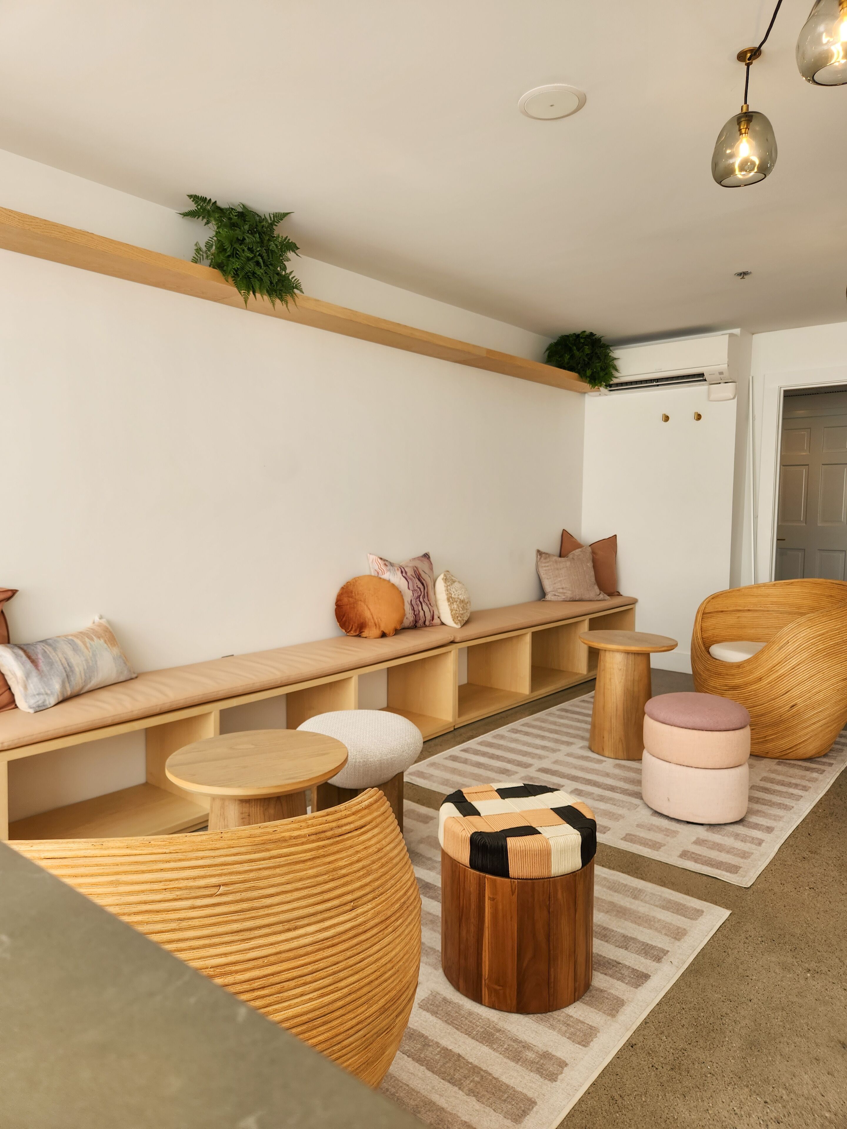 A modern living room with a wooden bench, round wooden tables, and a woven chair.