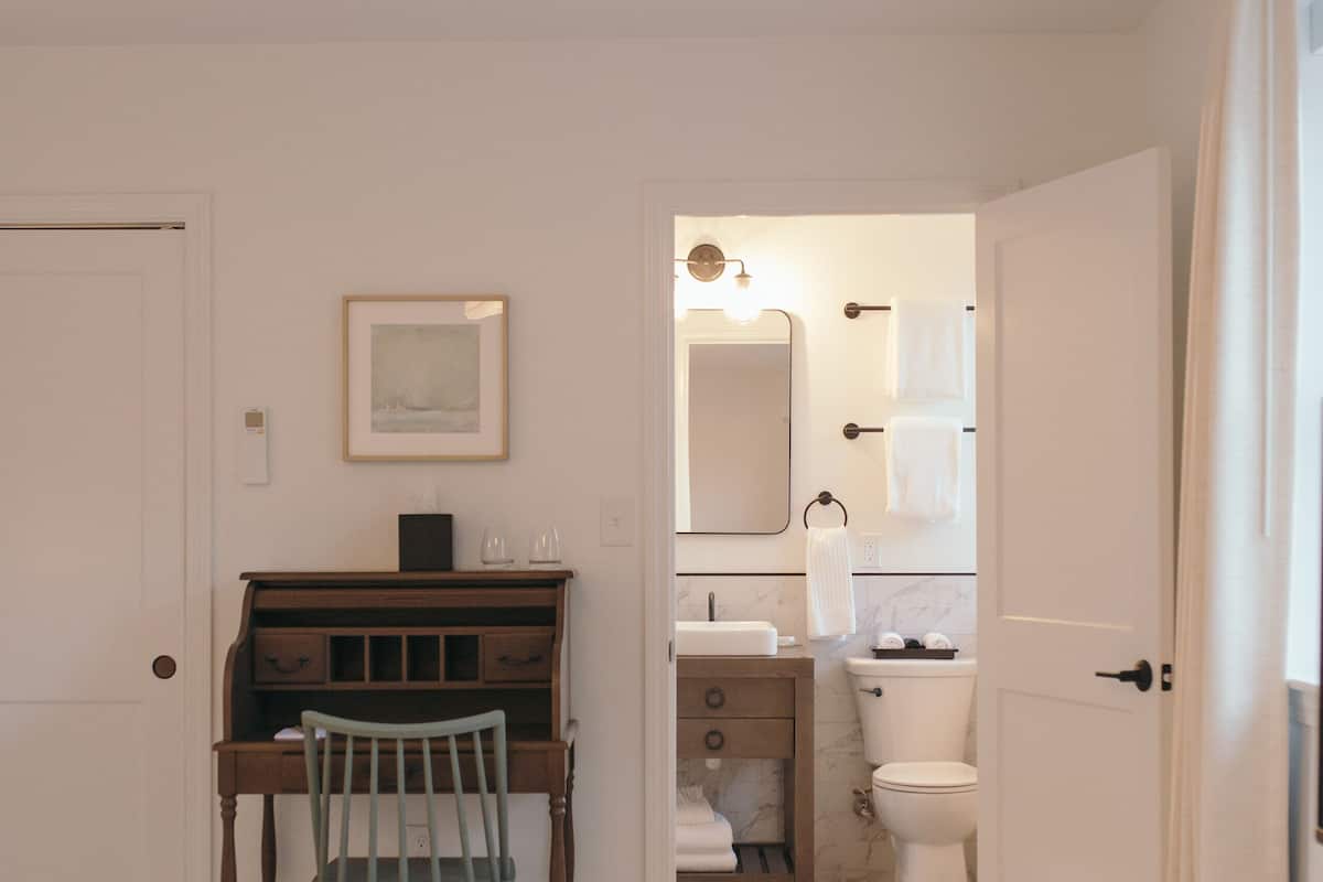 A bedroom with a bed, a desk, a chair, and a bathroom with a toilet and sink.