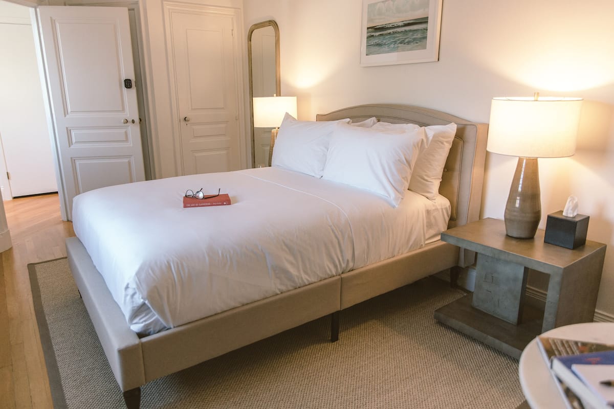 A neatly made bed with a headboard, bedside lamps, and a bedside table with a vase and tissue box.