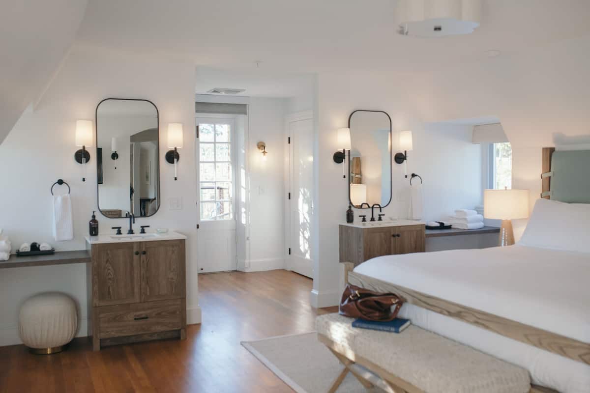A bedroom with a large bed, a wooden dresser, a vanity with a mirror, and a nightstand with a lamp.
