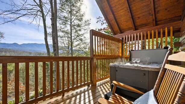 Une terrasse en bois avec un jacuzzi, un banc et une vue sur les montagnes.