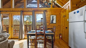 L’intérieur d’un chalet en bois comprend une table à manger pour quatre personnes, des chaises en bois, un lustre, un réfrigérateur et un extincteur.