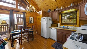 Une cabane en bois comprenant un coin repas, une cuisine et offrant une vue sur l’extérieur.