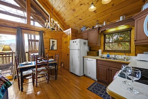 A wooden cabin with a dining area, kitchen, and a view of the outdoors.
