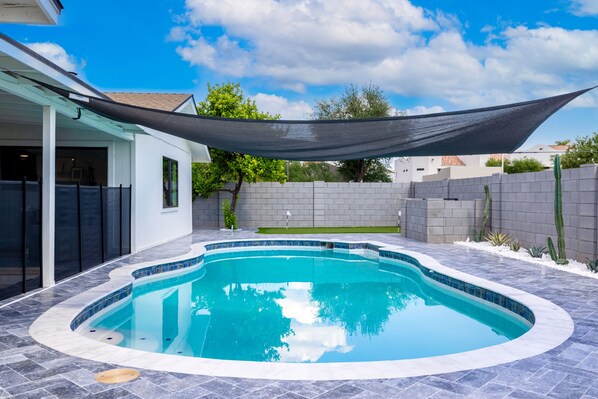 A swimming pool with a curved edge, surrounded by a tiled patio.