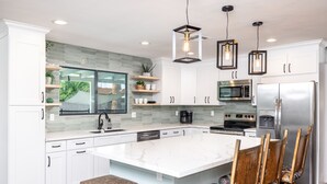 A modern kitchen with white cabinets, a large island, and pendant lighting. - Stay & Play: Heated Pool, Putting Green, and Games (Tempe)