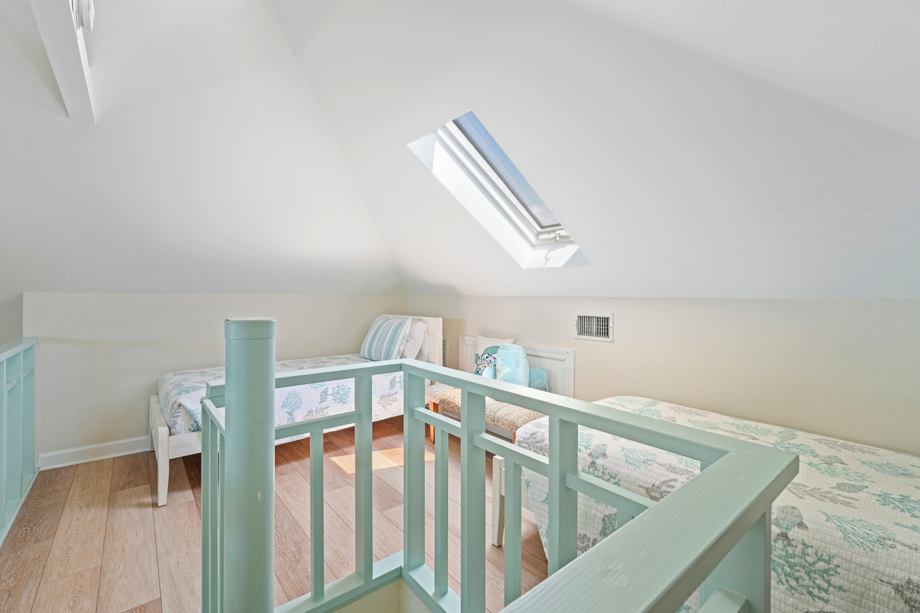 Un dormitorio con techo inclinado, tragaluz, cama con ropa de cama floral y una mesita.