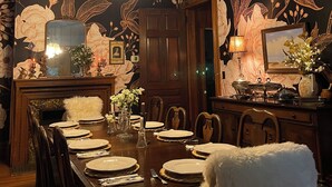 Une salle à manger agrémentée d’un lustre, d’un papier peint à motifs floraux et d’une table à manger en bois, mise pour le repas.