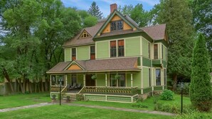 Une maison à deux étages avec un porche, entourée d’une pelouse bien entretenue et d’arbres.