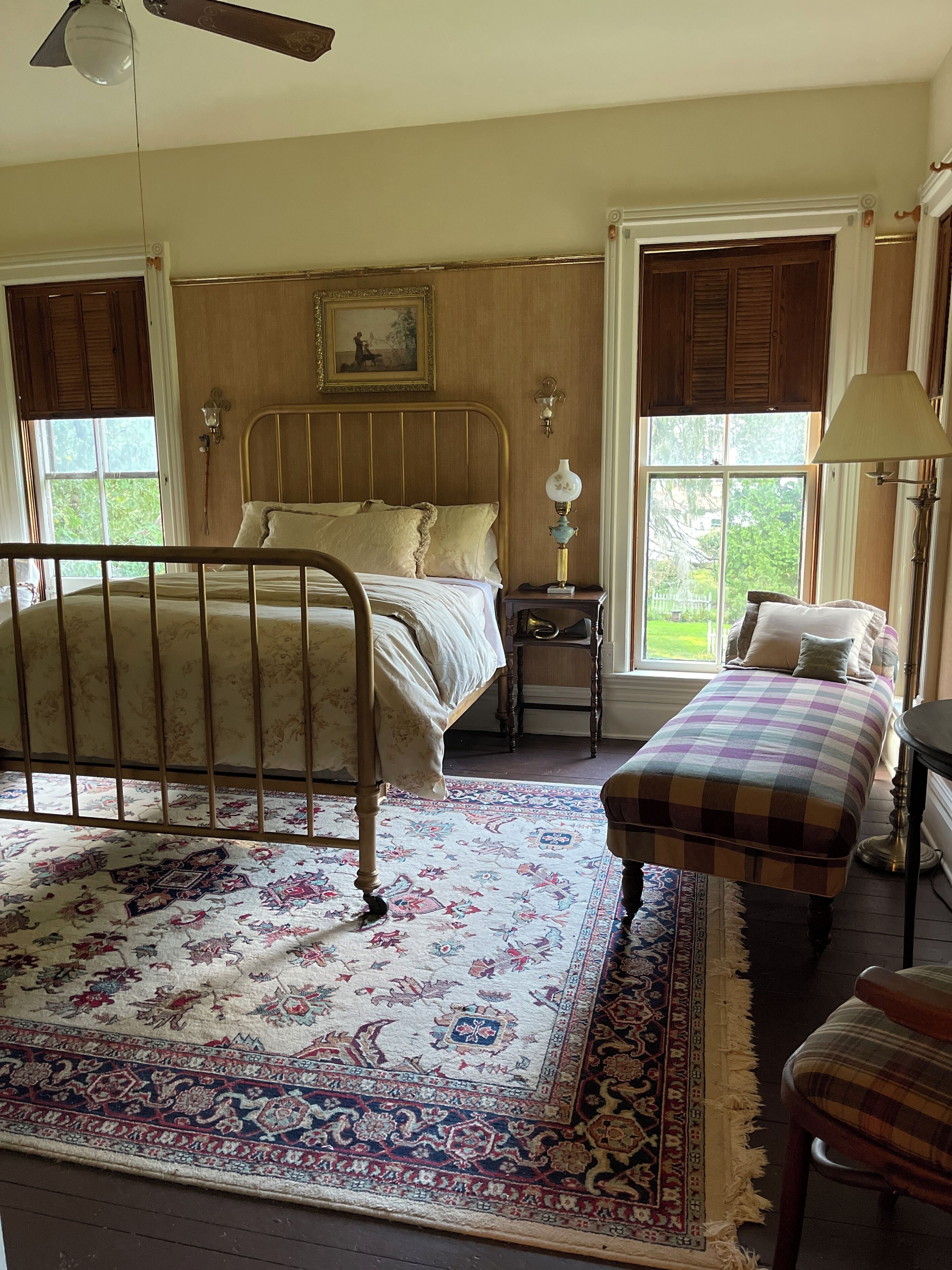 A bedroom with a wooden bed, a bench, a nightstand, and a window with shutters.