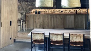 Een landelijke keuken met stenen muren, houten balken en een grote houten tafel met stoelen.