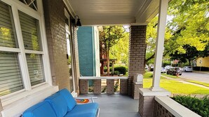 A covered porch with a blue lounge chair, a brick wall, and a view of the street. - Historic 155 y/o 3-bedroom KC house with hot tub. (Kansas City)