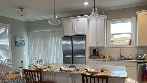 A modern kitchen with white cabinets, stainless steel appliances, and a central island with bar stools. - Downtown Coastal Craftsman Escape close to Riverwalk, Amphitheater, Beaches!! (Wilmington)