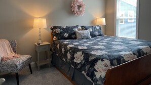 A bedroom with a bed, two bedside lamps, a chair, a decorative wall piece, and a window with blinds. - Downtown Coastal Craftsman Escape close to Riverwalk, Amphitheater, Beaches!! (Wilmington)