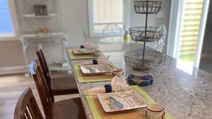 A kitchen with a granite countertop, wooden chairs, and a dining table set with placemats and ceramic dishes. - Downtown Coastal Craftsman Escape close to Riverwalk, Amphitheater, Beaches!! (Wilmington)