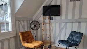 A room with a TV mounted on the wall, a fan, and two chairs.