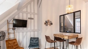 A room with a loft-style ceiling, a flat-screen TV mounted on a wooden ladder, a dining table with four chairs, and a large mirror on the wall.