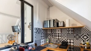 A compact kitchen with a black and white patterned backsplash, a wooden countertop, a sink, and a small shelf with kitchen appliances.