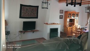 A living room with exposed wooden beams, a fireplace, a mounted television, and a wooden cabinet.