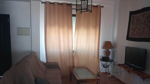 A living room with a sofa, a small table, a lamp, and a TV on a stand.