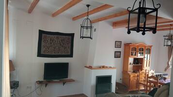 A living room with exposed wooden beams, a fireplace, a mounted television, and a wooden cabinet.