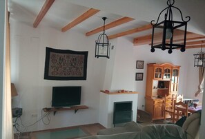 Sala de estar com vigas de madeira aparentes, lareira, televisão montada e um armário de madeira.