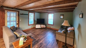 Ein gemütliches Wohnzimmer mit Holzböden und hoher Decke, ausgestattet mit zwei Sofas, einem Couchtisch, einem Fernseher und einer Lampe.