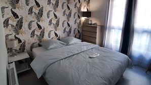 Een slaapkamer met een bed, een nachtkastje met lamp, een dressoir en een raam met gordijnen.