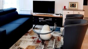 Een moderne woonkamer met een flatscreen televisie, een blauwe bank, een salontafel en een kamerkleed met een patroon.