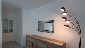 Een kamer met een houten dressoir, een spiegel en een vloerlamp.