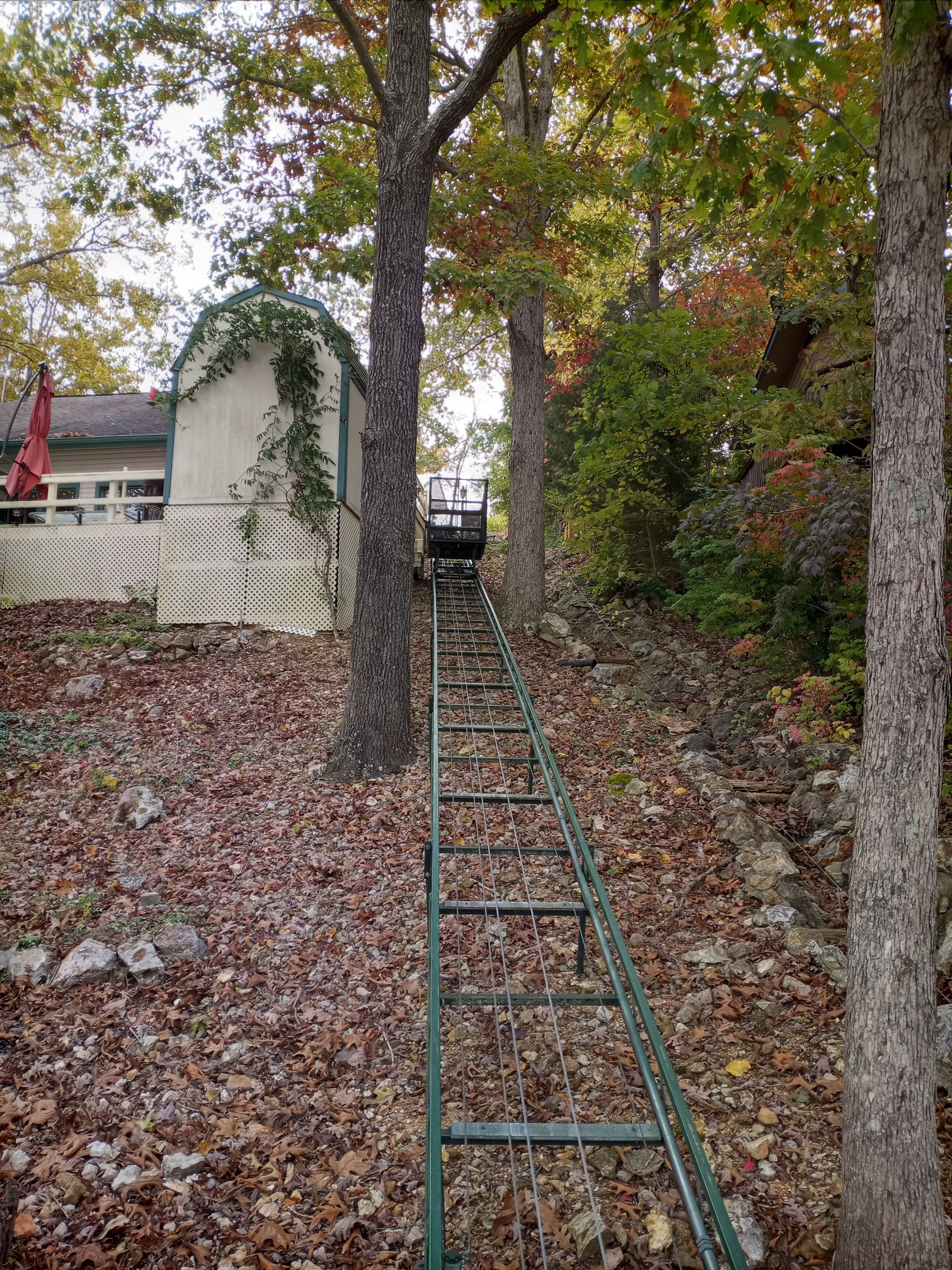 A metal staircase leading up a hill, surrounded by trees and a white fence.