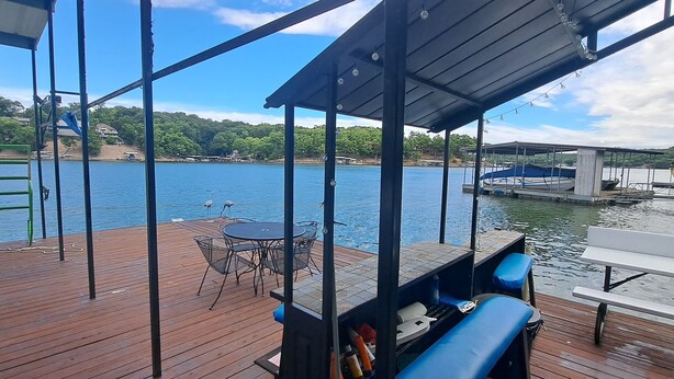 Eine Holzterrasse mit Tisch und Stühlen, mit Blick auf ein Gewässer mit einem Steg und einem überdachten Bereich.