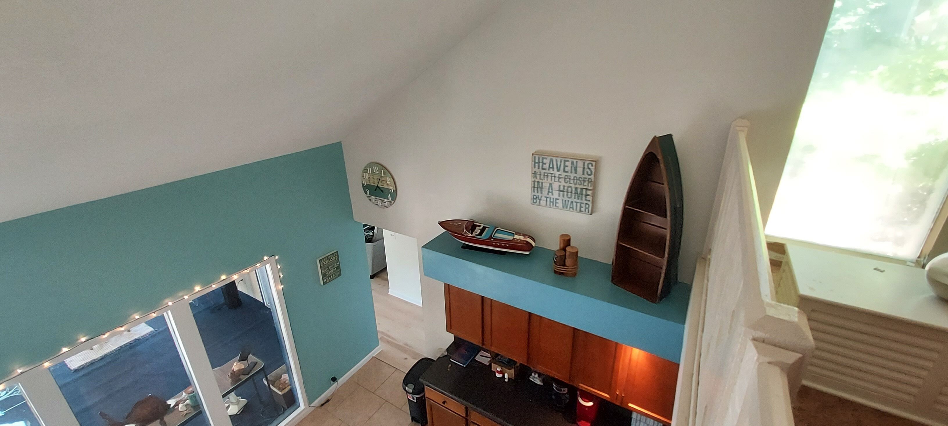 A room with teal walls, a wooden counter, a clock, a surfboard, and a sign that says "Heaven is a little closer in a home by the water."