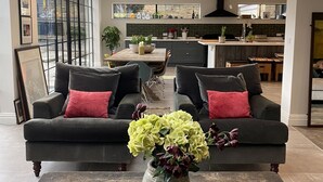 A modern living room with two dark sofas, a coffee table with a vase of flowers, and a large window overlooking a garden. - Grand open plan modern home with heaps of light, and close to London (Kingston upon Thames)