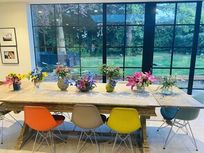 A dining area with a long table, colorful chairs, and multiple flower arrangements. - Grand open plan modern home with heaps of light, and close to London (Kingston upon Thames)