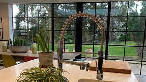 A modern kitchen with a large window, a stainless steel sink, and potted plants. - Grand open plan modern home with heaps of light, and close to London (Kingston upon Thames)