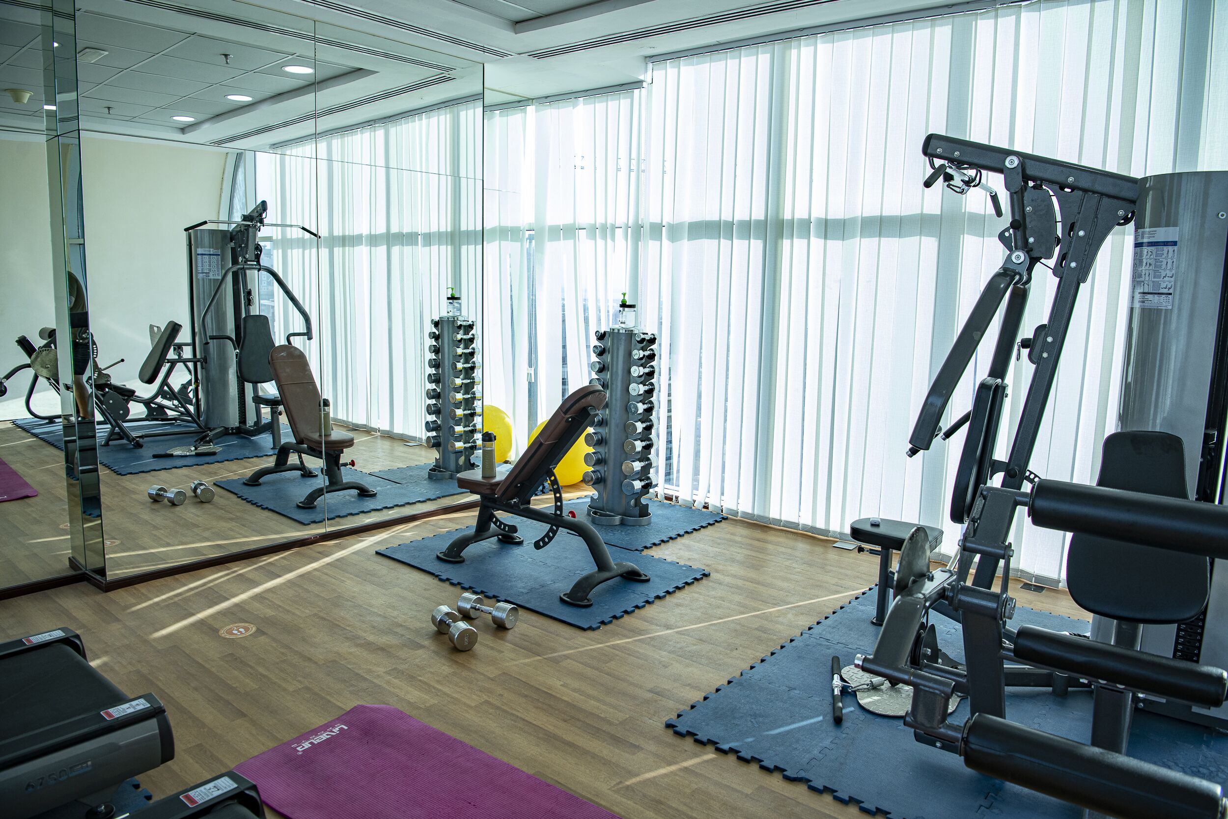 Une salle de sport équipée de divers appareils d’exercice, notamment des machines de musculation et des poids libres, disposés sur des tapis.