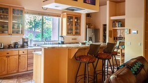 Een ruime keuken met houten kastjes, een groot eiland met barkrukken en uitzicht op de omgeving.
