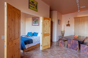 Une chambre à coucher avec un lit, une porte en bois et un coin repas comprenant une table et des bancs.
