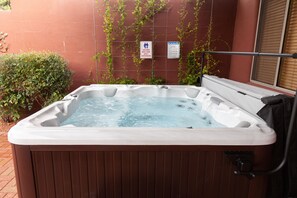 Ein Whirlpool mit Holzverkleidung, umgeben von einer Backsteinmauer und Grünpflanzen.