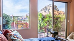 Een slaapkamer met een groot raam dat uitzicht biedt op een bergachtig landschap en een terras met buitenmeubilair.