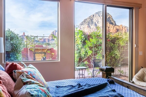 Ein Schlafzimmer mit großem Fenster und Blick auf eine Berglandschaft sowie einer Terrasse mit Gartenmöbeln.